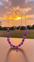 Purple bead necklace with multicolored purple and black glass beads, gold tone bead caps, and gold link chain.